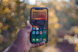 Image of a person's hand holding a smartphone against an outdoor bokeh background.